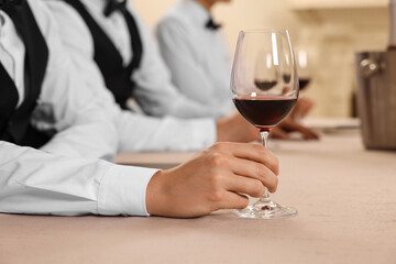 People with glasses of red wine at table indoors, closeup. Professional butler courses