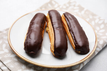 Delicious eclairs covered with chocolate on grey table, closeup