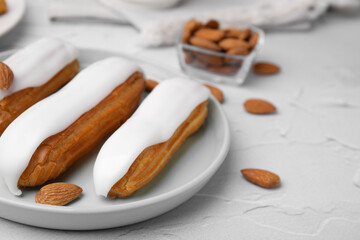Delicious eclairs covered with glaze and almonds on white textured table, closeup. Space for text
