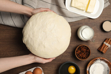 Woman holding fresh yeast dough at wooden table, top view. Making cake