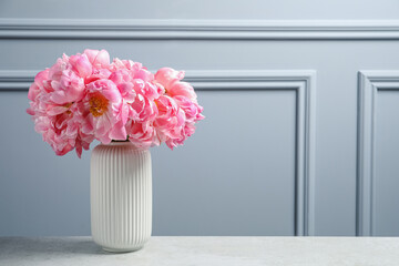 Beautiful bouquet of pink peonies in vase on table near grey wall. Space for text