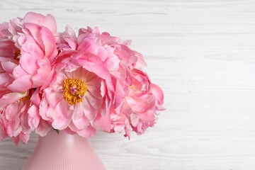 Beautiful bouquet of pink peonies in vase on white wooden background, closeup. Space for text