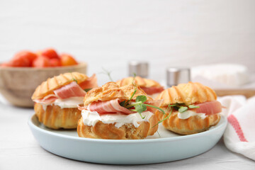 Delicious profiteroles with cream cheese and prosciutto on white table, closeup