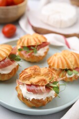 Delicious profiteroles with cream cheese and prosciutto on plate, closeup