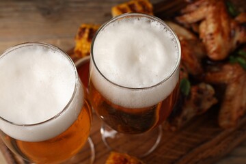 Glasses with beer and delicious baked chicken wings on table, closeup
