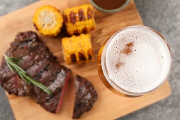 Glass of beer, delicious fried steak and corn on grey table, top view. Space for text