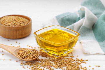 Bowl of natural oil and mustard seeds on white wooden table