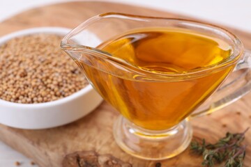 Jug of natural oil and mustard seeds on wooden table, closeup