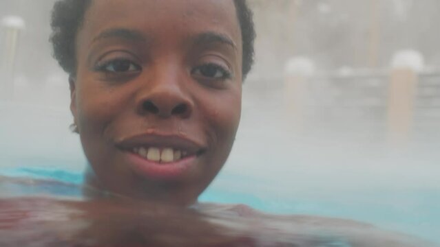 Close-up portrait of charming African American woman relaxing in hot water on winter day smiling at cameraClose-up portrait of charming African American woman relaxing in hot water on winter day smili