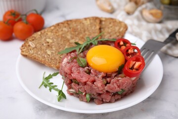 Tasty beef steak tartare served with yolk, pepper, bread and greens on white marble table