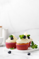 Cupcakes, muffins decorated with cream, berries and green mint leaves. Delicious homemade dessert. Pastry.
