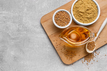 Jug of natural oil, mustard seeds and powder on grey table, top view. Space for text