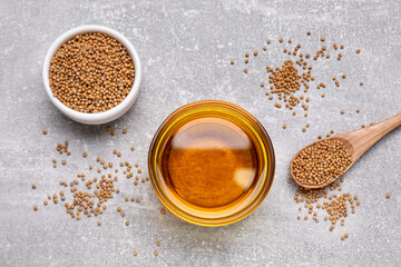 Bowl of natural oil and mustard seeds on light grey table, flat lay