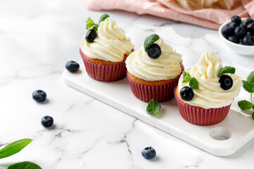 Decorated muffins, cupcakes with cream, blueberries and green mint leaves. Delicious homemade...