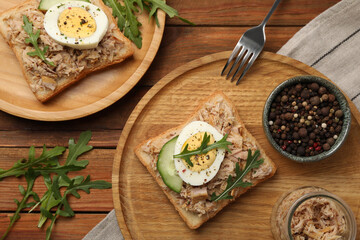 Delicious sandwiches with tuna, greens, cucumber, boiled egg and ingredients on wooden table, flat lay