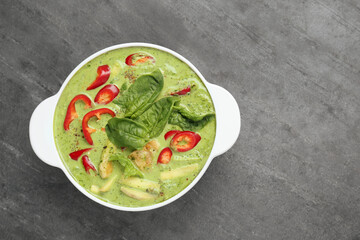 Saucepan with delicious green curry chicken soup on light grey table, top view. Space for text