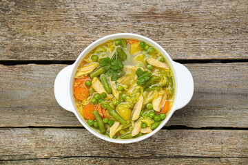Saucepan of delicious vegetable soup with chicken on wooden table, top view