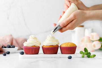 Making, decorating cupcakes, muffins with cream, blueberries and green mint leaves. Delicious...