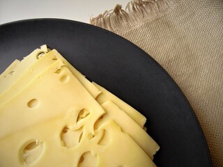 Dutch Maasdam cheese on a gray plate against a background of rough cloth