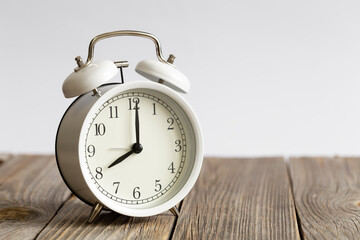 White alarm clock on a wooden surface close-up, blurred white background, space for text, concept of morning, deadline, time management.