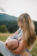 Mother feeding breast newborn baby sitting on the grass in the park. World Breastfeeding Week. Mom...