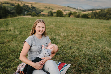 Mother feeding breast newborn baby sitting on blanket on grass in the park. World Breastfeeding...