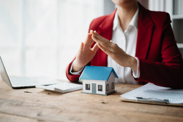 Female real estate agent is use hands to protect red roof for the concept of real estate investment about house trading, purchase at desk in office .