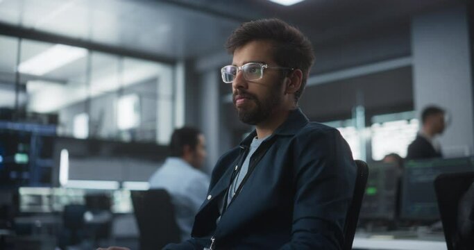 Handsome Indian Software Developer Working on Computer in a Technological Laboratory Environment. Young Man is Thoughtful at His Workplace, Drafting Research Ideas for an AI Development Blockchain
