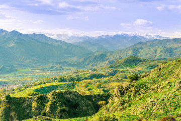 picturesque view in a green mountain valley among slopes and hills with sunny plantations on a rocky plato and nice cloudy sunset on background