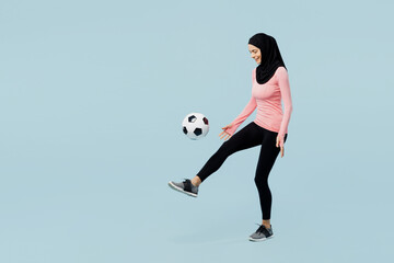 Full body young asian muslim fitness trainer sporty woman wear pink abaya hijab spend time in home gym kicks soccer ball on foot isolated on plain blue background studio Workout sport fit abs concept