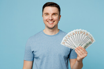 Young satisfied smiling cheerful happy man wear casual t-shirt hold in hand fan of cash money in...