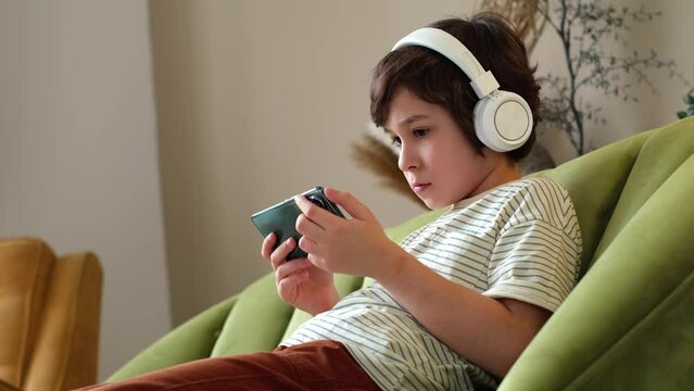 young boy sits cozily on a sofa, completely absorbed in his smartphone. The child is fully engrossed in the digital realm before him. impact of modern technology and the digital world on children's
