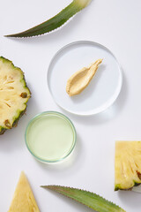 A yellow cream texture on transparent podium, essence on petri dish, fresh pineapple slices and green leaves decorated on white background. Scene for advertising cosmetic product of pineapple extract.