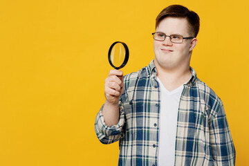 Young smiling man with down syndrome wears glasses casual clothes using hold magnifying glass...