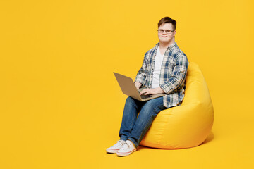 Full body young IT man with down syndrome wears glasses casual clothes sit in bag chair hold use...