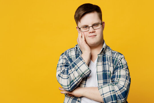 Young sad minded pensive man with down syndrome wearing glasses casual clothes looking camera prop up forehead head isolated on pastel plain yellow color background. Genetic disease world day concept.