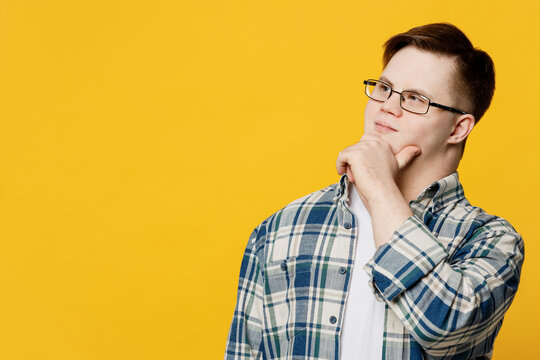 Young minded thoughtful man with down syndrome wearing glasses casual clothes looking aside on area props up chin isolated on pastel plain yellow color background. Genetic disease world day concept. - Powered by Adobe