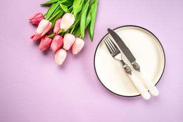 Festive creative table setting plate and tulip bouquet on purple background. Women's Day and Mother's Day
