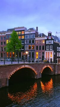 Night view of Amsterdam cityscape with canal, bridge and medieval houses in the evening twilight illuminated. Amsterdam, Netherlands
