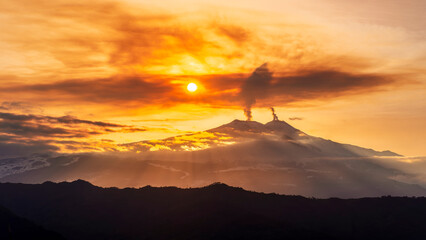 mysterious landscape of great erupting volcano with smoke from craters and snow on slopes in orange...