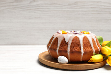 Delicious Easter cake decorated with sprinkles near egg and beautiful tulips on white wooden table. Space for text
