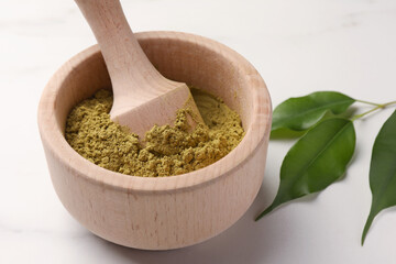 Mortar of henna powder and green leaves on white marble table, closeup. Natural hair coloring