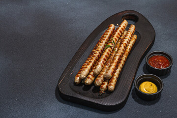 Roasted pork meat sausages on wooden board. Set of sauces, traditional food for picnic or BBQ