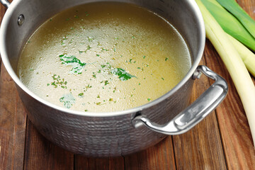 Pot with tasty bouillon and celery on wooden table, closeup