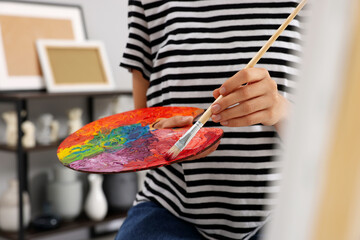 Young woman mixing paints on palette with brush in studio, closeup