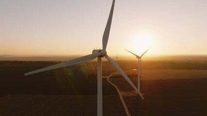 Alternative energy large wind turbines with blades in field aerial view bright orange sunset blue sky wind park slow motion drone turn. Silhouettes windmills, large orange sun disc summer lens flare - Powered by Adobe