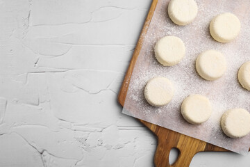 Wooden board with uncooked cottage cheese pancakes on white textured table, top view. Space for text