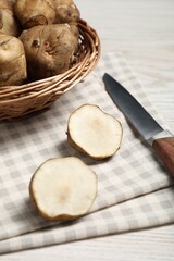 Wicker basket and many Jerusalem artichokes with knife on white wooden table