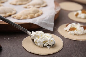 Process of making dumplings (varenyky) with cottage cheese. Raw dough and ingredients on brown table, closeup