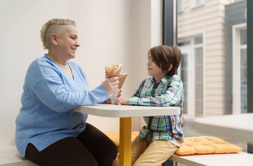 Cheerful white woman with short hair feeding her little boy in a Greek fast food restaurant. Mother...